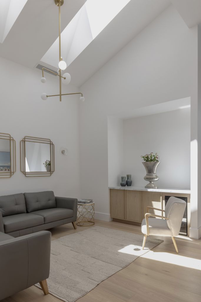 Living area with vaulted ceiling, skylights, gold-framed mirrors, grey leather sofas and timber sideboard