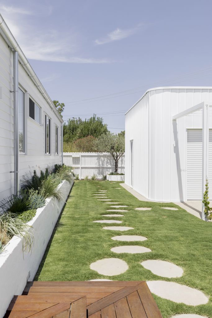 Side garden walkway with stepping stones across lawn, garden beds and white rendered outbuilding