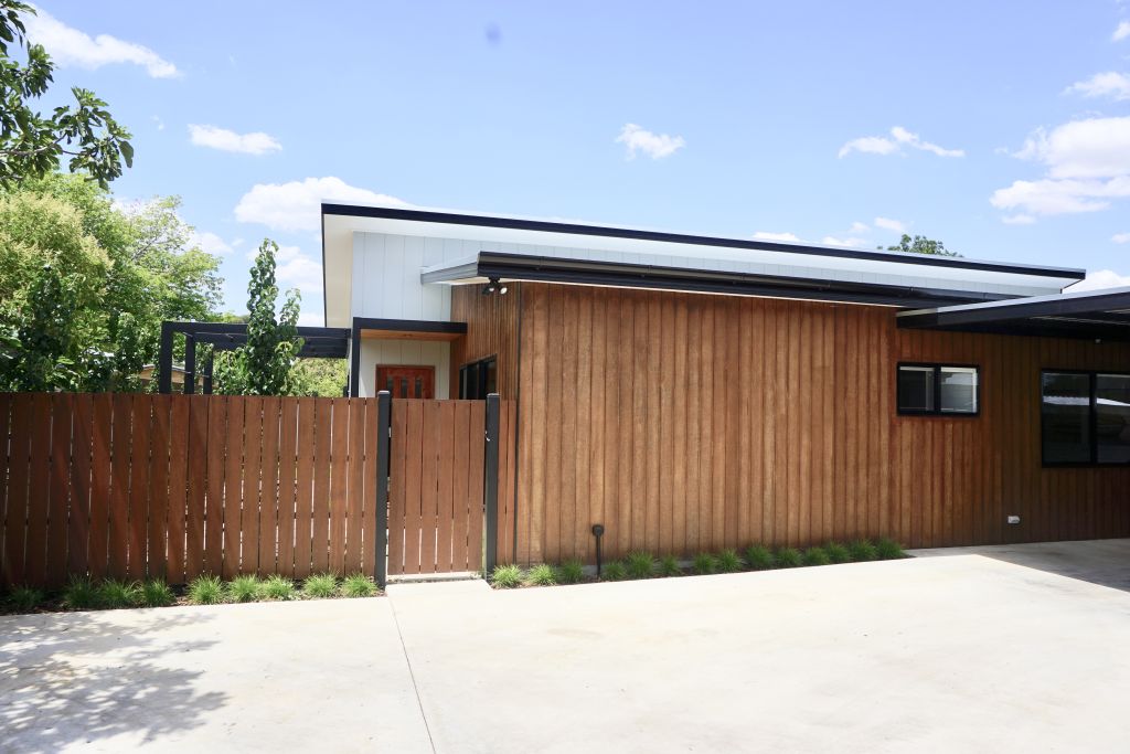 Exterior of home featuring timber cladding, white gable, timber gate and fence, and driveway