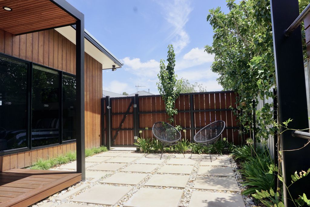 Outdoor courtyard with paved stepping stones, wicker-style chairs, timber screening and garden bed
