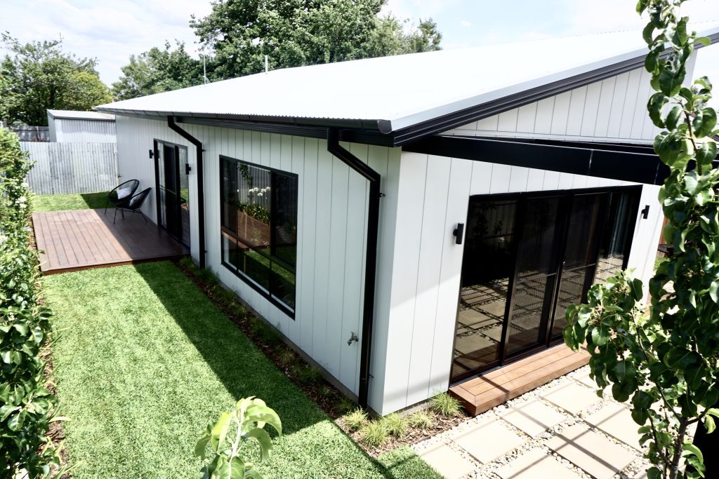 Exterior view of skillion-roofed home with white cladding, black-framed windows and outdoor deck