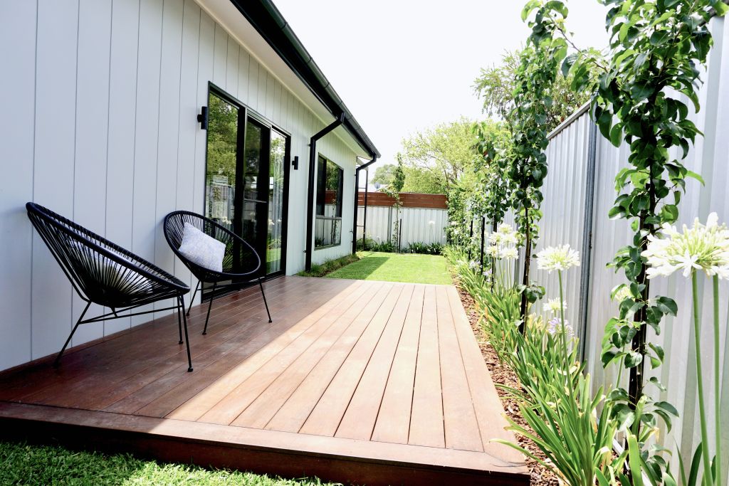 Timber deck with outdoor chairs, side garden path bordered by agapanthus and corrugated fencing