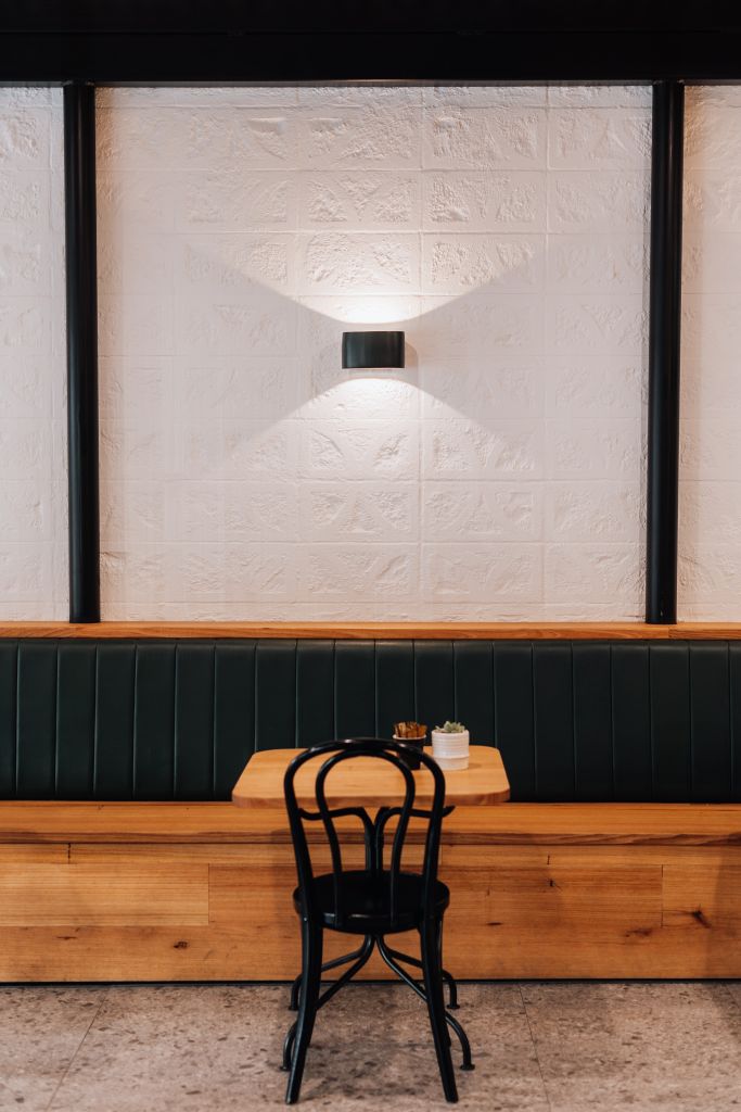 Café booth seating with green leather banquette, timber table, bentwood chair and wall sconce lighting