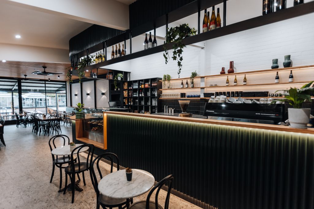 Café interior with espresso bar, mezzanine bottle display, marble bistro tables and bentwood chairs