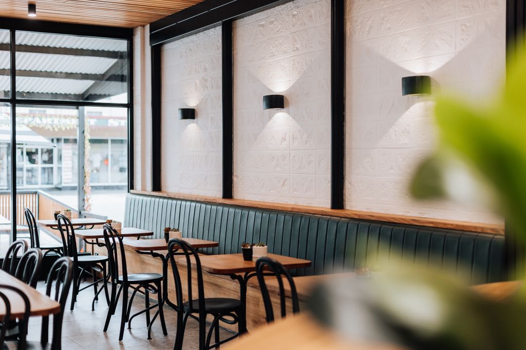 Café dining area with green leather banquette seating, timber tables, bentwood chairs and feature wall lighting
