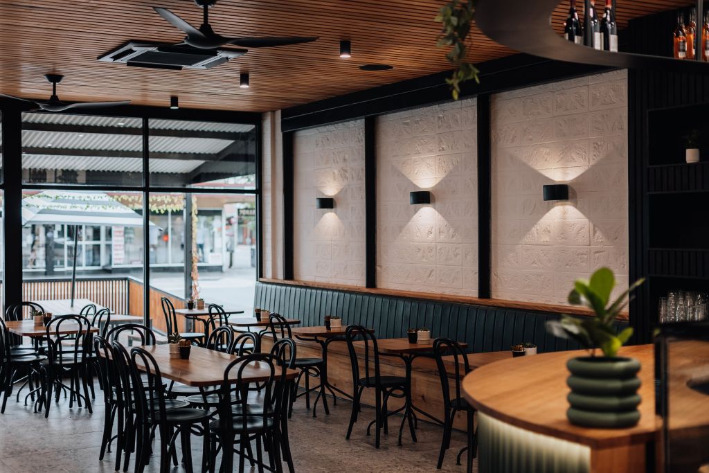 Café dining area with timber tables, black bentwood chairs, ceiling fans and view to outdoor street seating