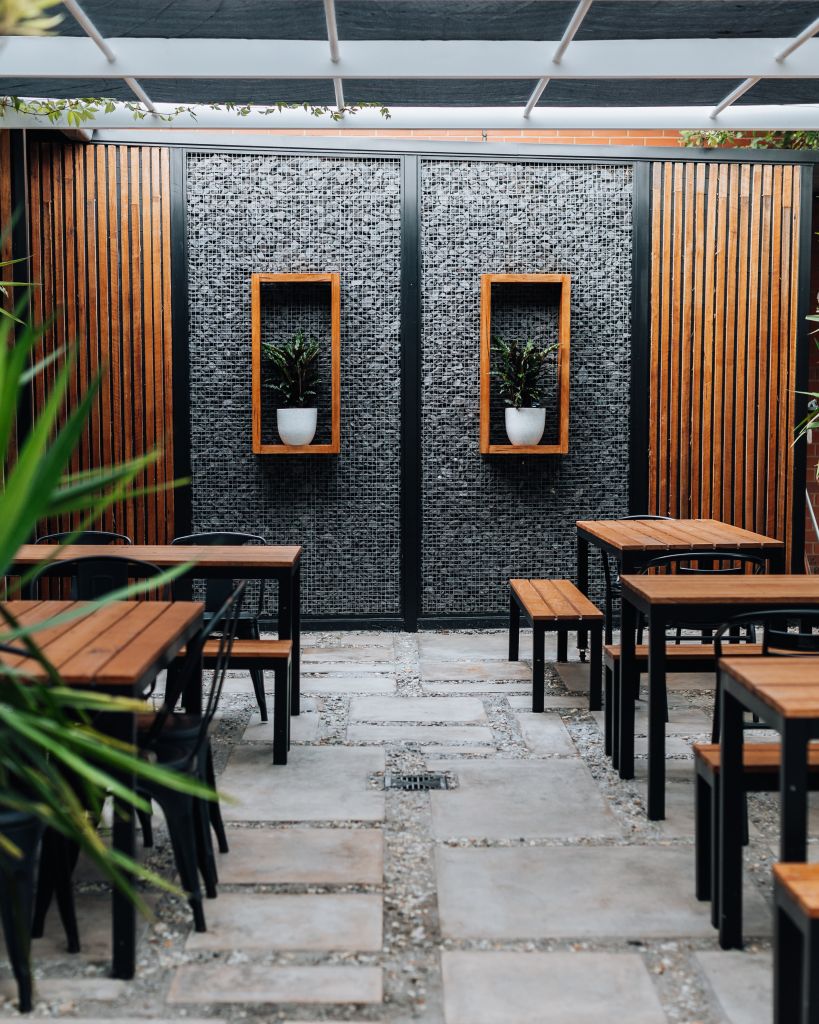 Outdoor courtyard with timber tables and benches, gabion stone feature wall and framed planter boxes