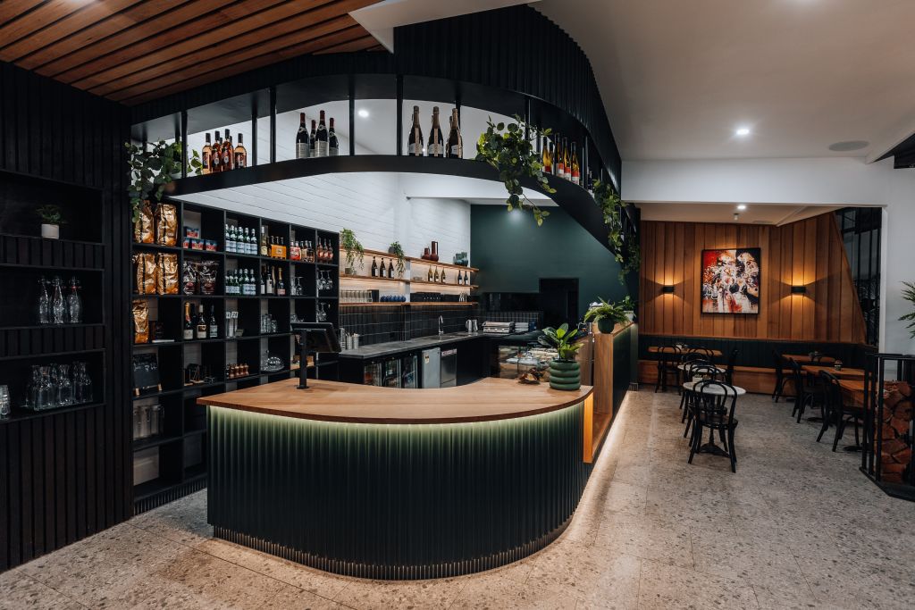 Interior of café/bar with curved timber-topped counter, mezzanine wine display and dining area